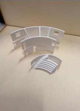 Two white 3D-printed section-model pieces: a curved wall segment with window openings and a curved tier of stepped seating.
