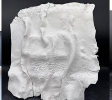 A square slab of white clay folded into an organic wrinkled surface, standing on a black ground.